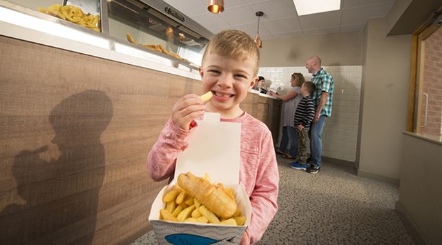 A boy tucking into a box of fish and chips at the takeaway