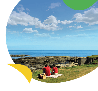 A couple sat on a cliff looking out to sea at Church Point Holiday Park