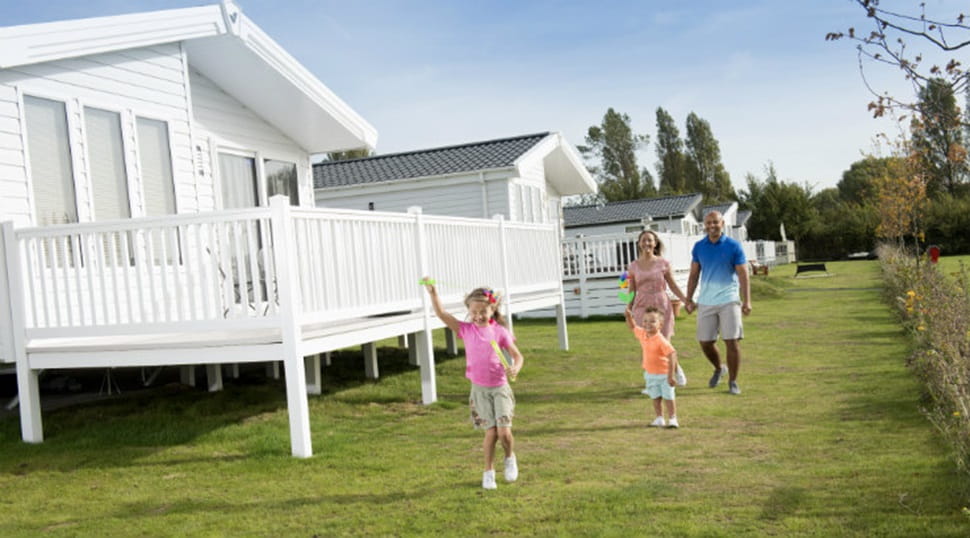 A family walking on the grass past the lodges at Coopers Beach Holiday Park