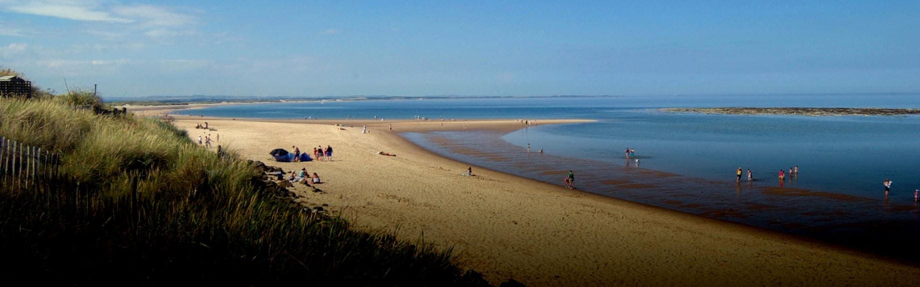 panoramic view of a sandy beach between green countryside and blue sea