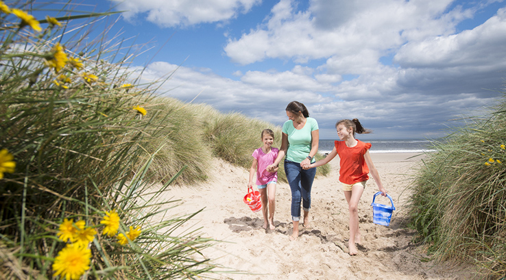 a family walking through the sand dunes at Cresswell Beach
