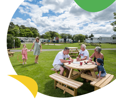 A family sat at a picnic table in the sun at Cresswell Towers Holiday Park