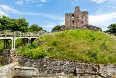 Stony ruins on top of a grassy hill against blue skies