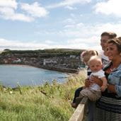 Couple with two small children sat on a wall looking out at a sea view