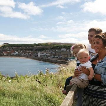 Couple with two small children sat on a wall looking out at a sea view
