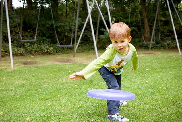 A child throwing a frisbee across the grass near the swings at Gatebeck Holiday Park
