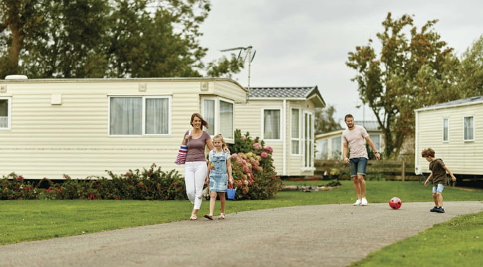 family walking past caravans with father and son kicking a football
