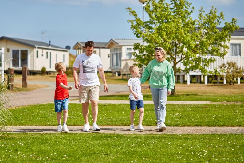 Family of four walking and smiling with holiday park in the foreground