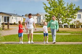 Family of four walking and smiling with holiday park in the foreground