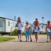 A family of five in a holiday park walking, two carrying children on their shoulders