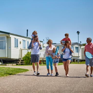 A family of five in a holiday park walking, two carrying children on their shoulders