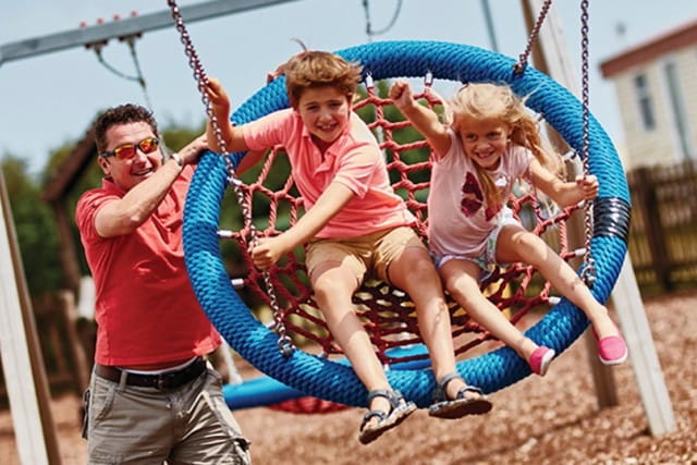 man pushing two children on a swing