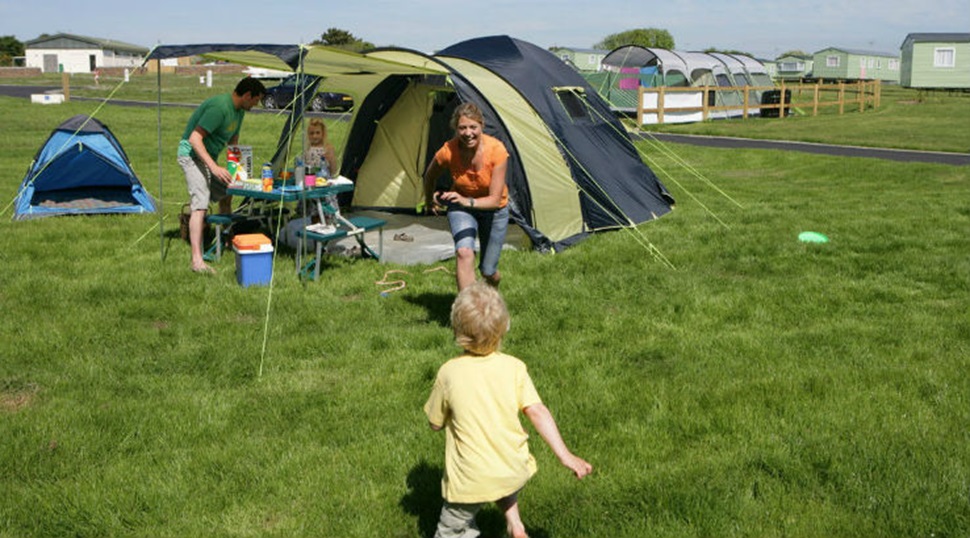 A family relaxing and playing games on the grass outside their tent