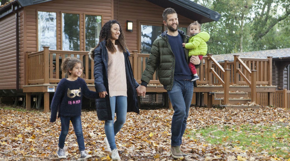 A family walking through autumn leaves outside a wooden lodge at Landguard Holiday Park