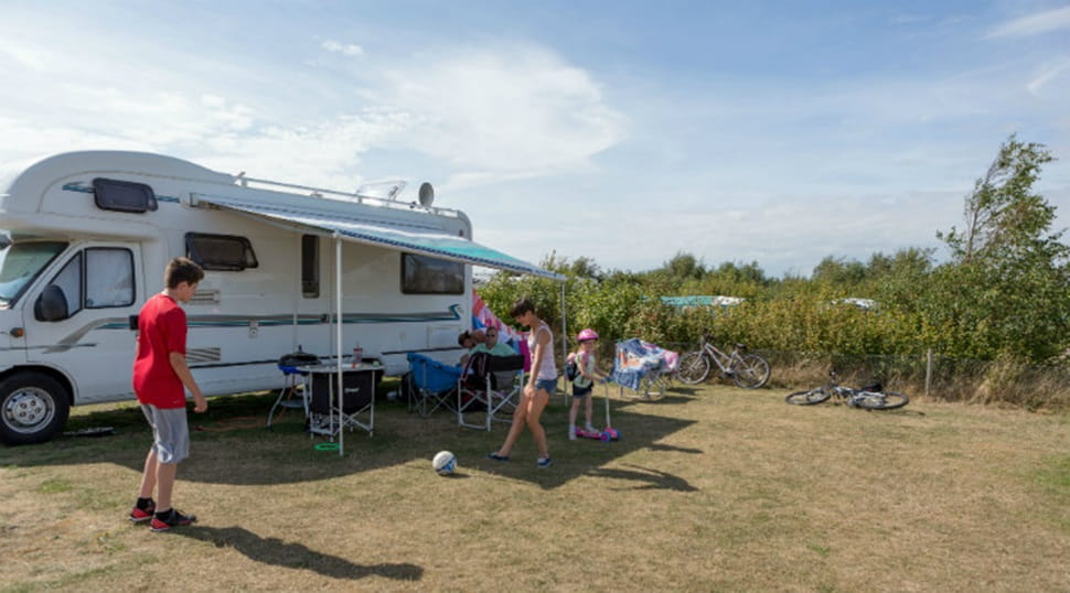 A family playing football on the grass outside their campervan