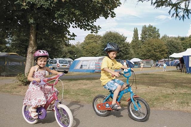 Two children riding bikes through the camp site at Landguard
