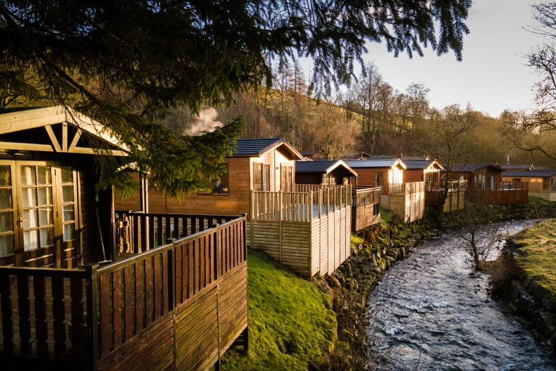 a river running past wooden lodge accommodation 