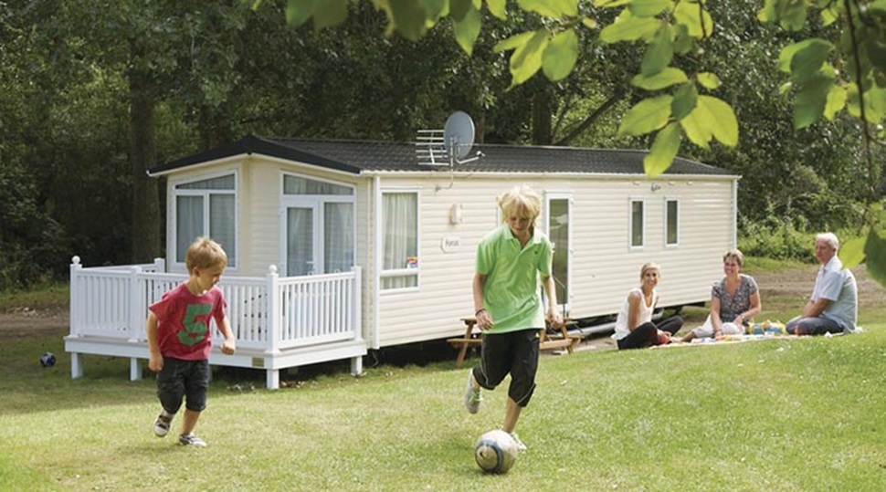 A father and son playing football and a family relaxing on the grass outside their caravan