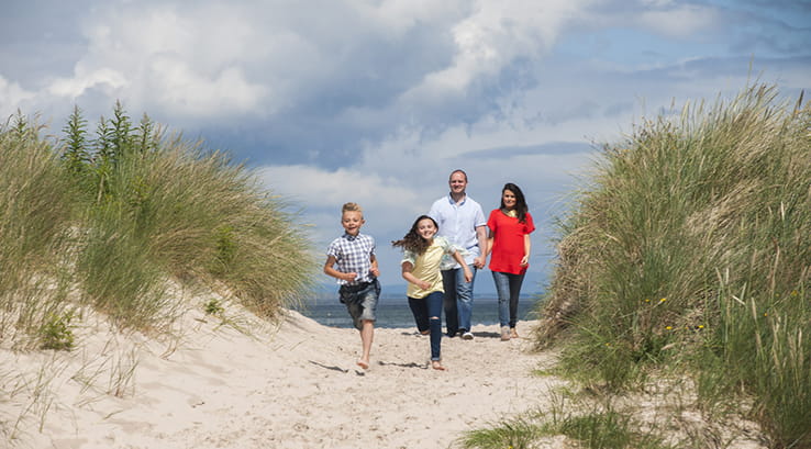 A family running down the sand dunes at Nairn Beach