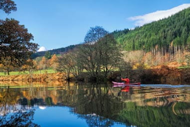 Picturesque loch and stunning woodland with person kayaking