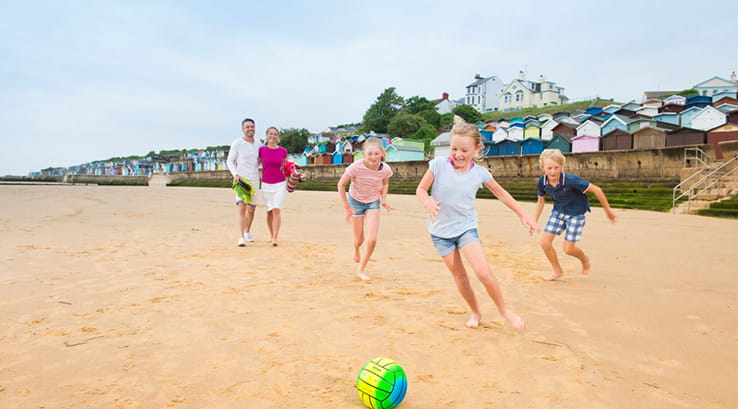 Kids playing football on the beach with parents walking in the background