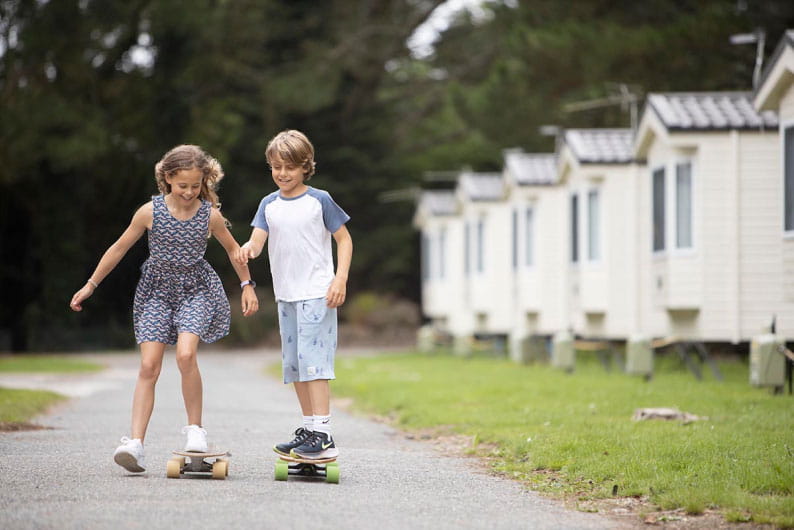 two children riding skateboards past caravans