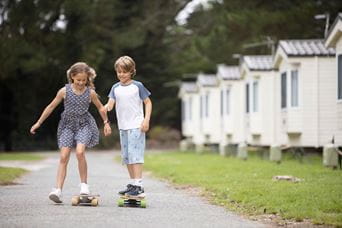 two children riding skateboards past caravans