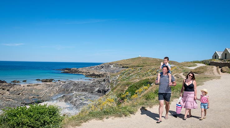 A family walking along a coastal path in the sun