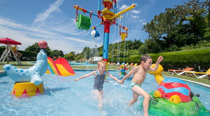 Children playing in an outdoor pool with slides in the background