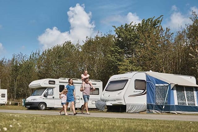 A family walking past touring caravans at Nodes Point