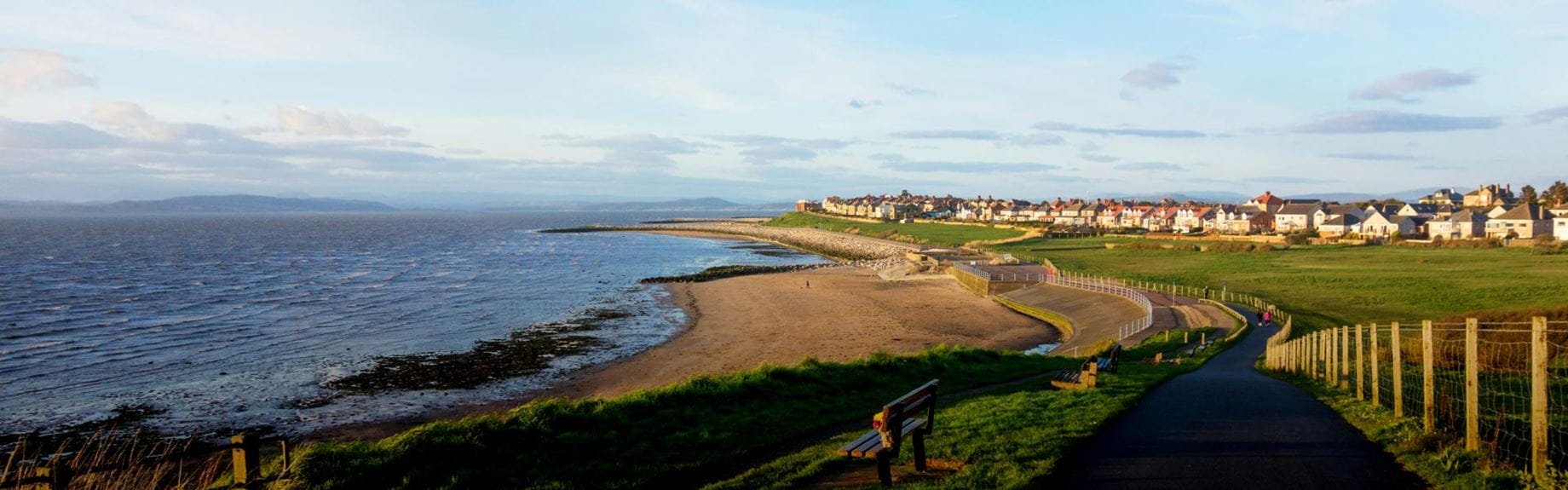 Path leading to grassy coastal town next to a beach