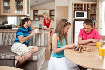 Children playing board games with parents stood in kitchen talking