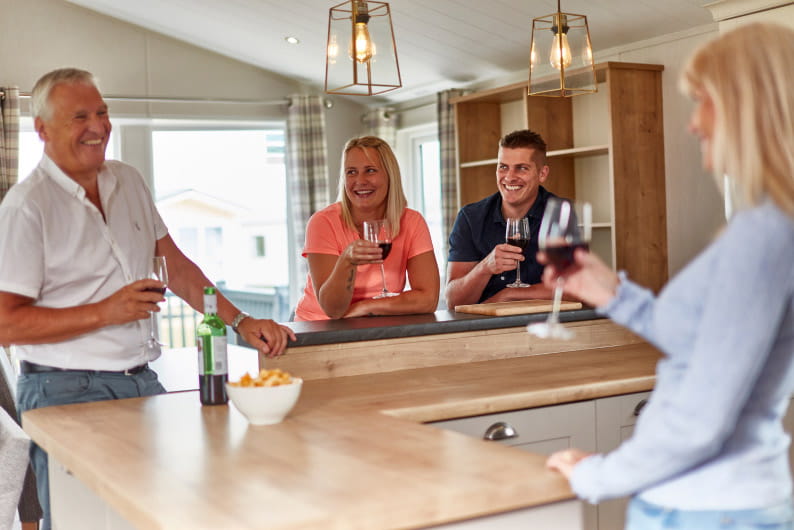 Two couples stood around kitchen island drinking red wine
