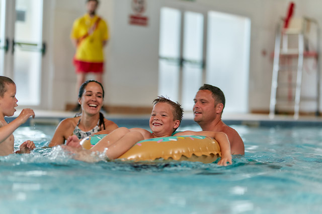 Parents with their kids in rubber rings in the indoor swimming pool at Pendine Sands