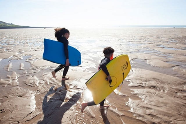 two children carrying body boards to the sea