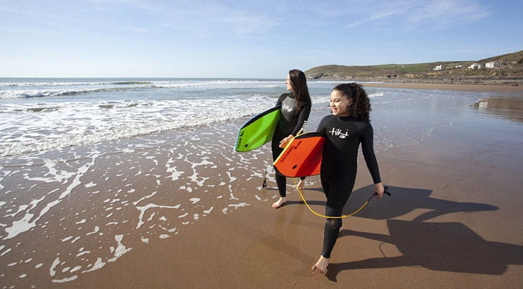 Two girls walking along Croyde Bay beach with surfboards