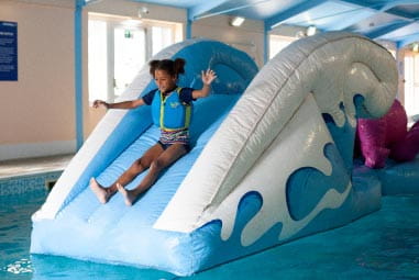 a young child in a life jacket sliding into a pool from an inflatable slide