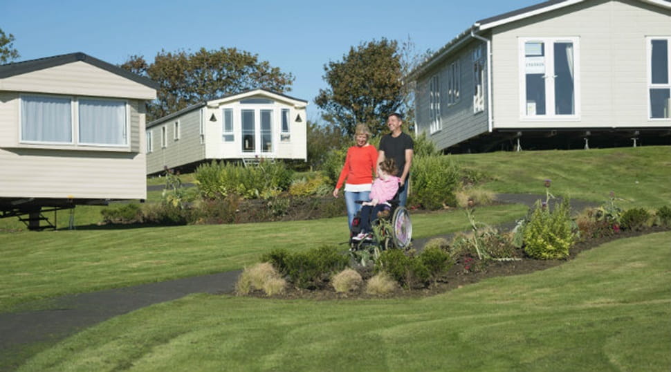 Parents wheeling their daughter in a wheelchair through the caravans at Sandy Bay Holiday Park