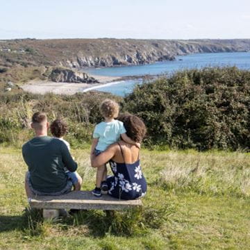 A family sitting on a bench looking out at the sea view