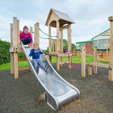 Two children playing on a metal slide in an outdoor adventure playground
