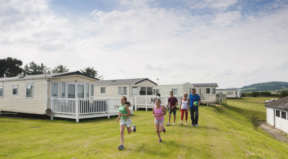 A family running along the grass alongside lodges at Southerness Holiday Park