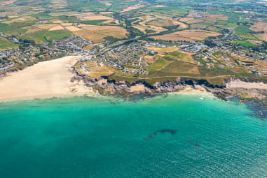 An aerial view over Polzeath surrounded by lush green fields, white sandy beaches and vibrant blue sea