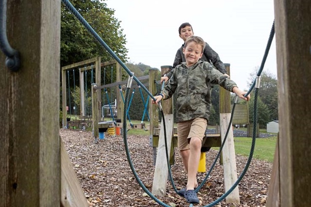 two boys walking along a rope bridge on the park