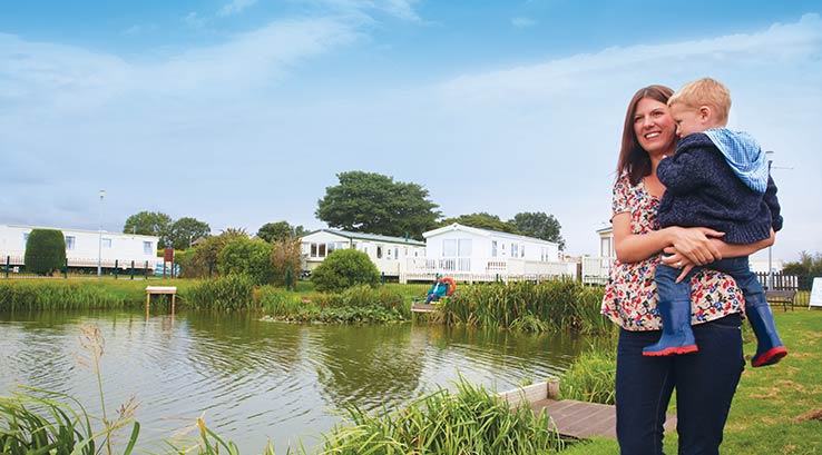 mother holding a young child next to a lake with caravans behind