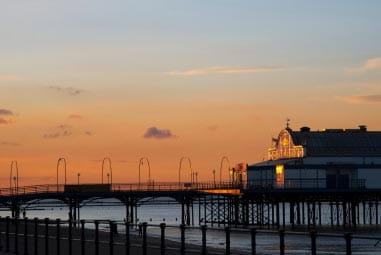 the sun setting behind a sea side peer