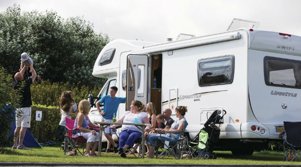 A family relaxing on the grass outside their campervan