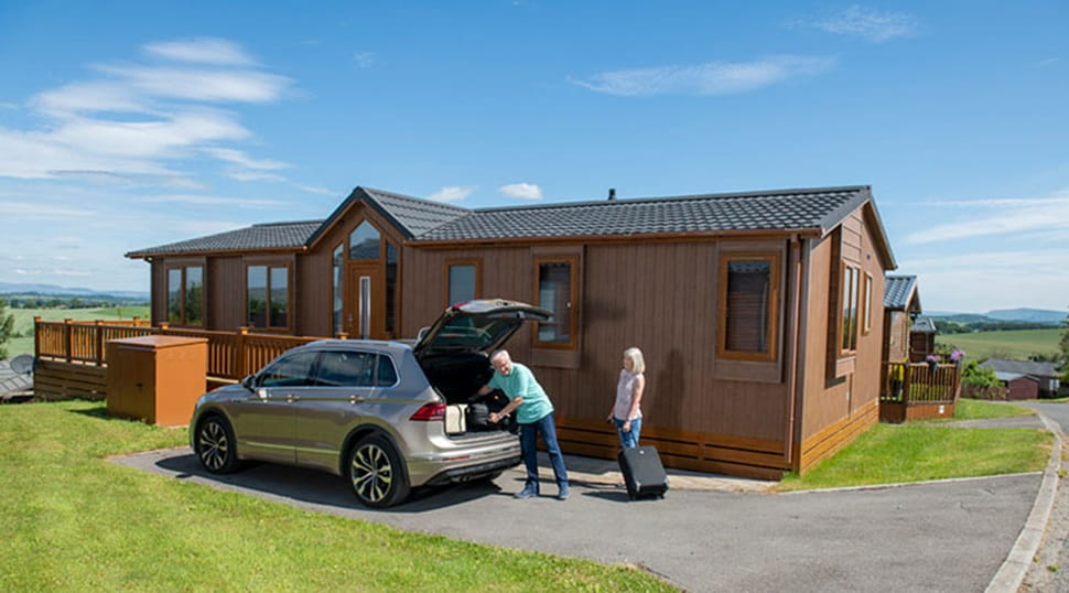 A couple unpacking their car outside their lodge at Todber Valley Holiday Park