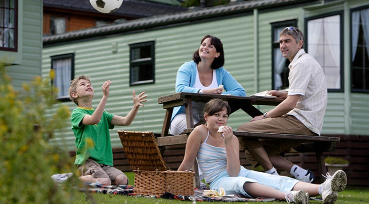 A family relaxing at a picnic table outside their holiday caravan at Todber Valley Holiday Park