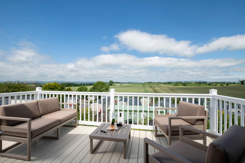Wooden terrace with seating, table and white railings with view of the countryside