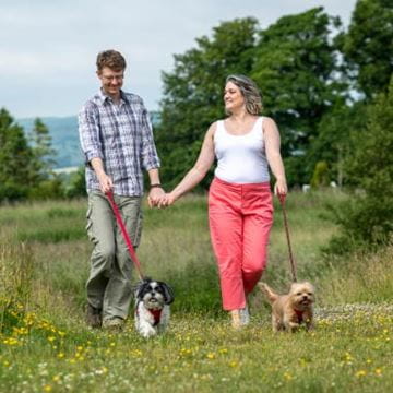 Couple holding hands both walking dogs on a red leash